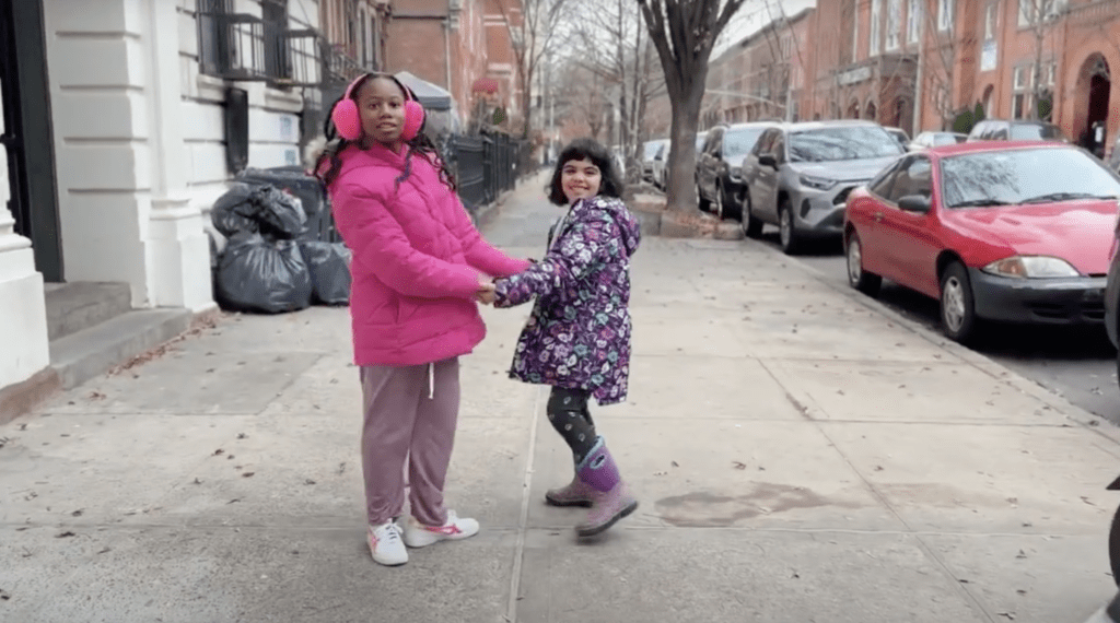 Noni and her sister Clementine hold hands on the sidewalk in New York City